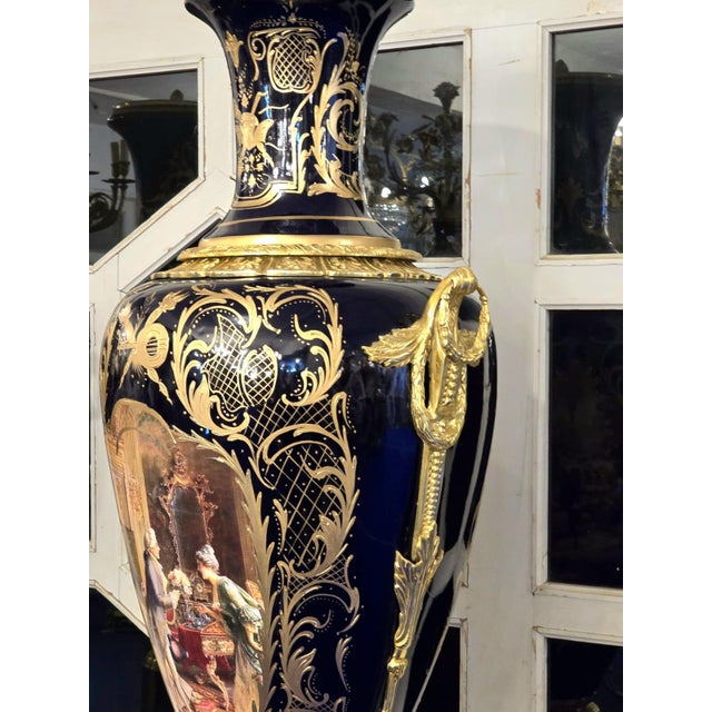 This monumental Sevres-style porcelain vase is a striking statement piece finished in deep midnight blue tones with lavish...
