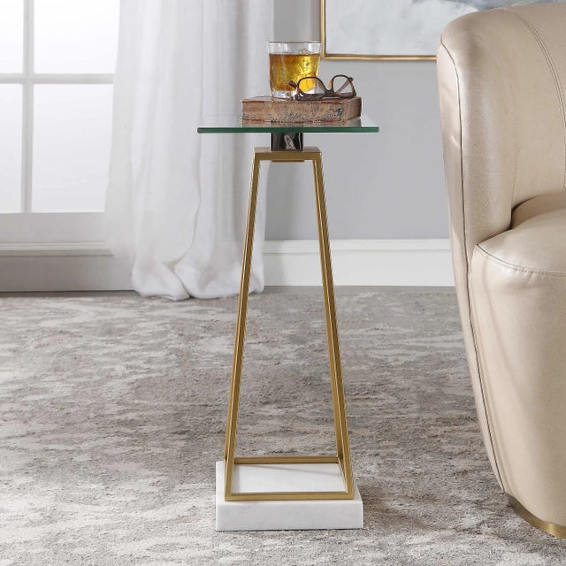 This linear designed metal accent table features a tapered open steel caged base finished in metallic gold leaf with a...