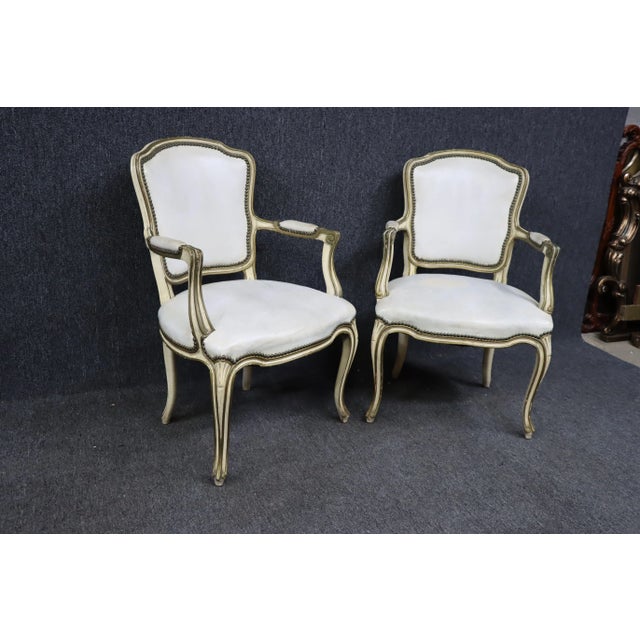A pair of Louis XV style open arm chairs , overall distressed appearance , white crackled leather upholstery, chippy cream...
