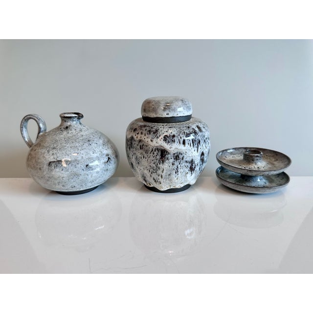 This handcrafted ceramic set, consisting of a lidded box, a handled vase, and two candlesticks, showcases the...