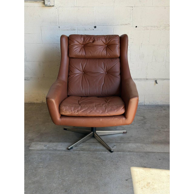 This swivel lounge chair features a curved shell upholstered in rich brown leather with tufted cushions. Its expressive...