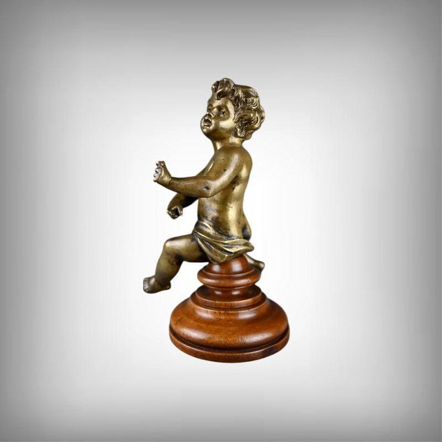 This small bronze Cupid, delicately patinated, rises on its polished wooden base like an apparition from an 18th-century...