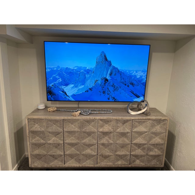 Modern sideboard is constructed from wood with a light natural finish. It has four doors featuring a geometric, diamond-...