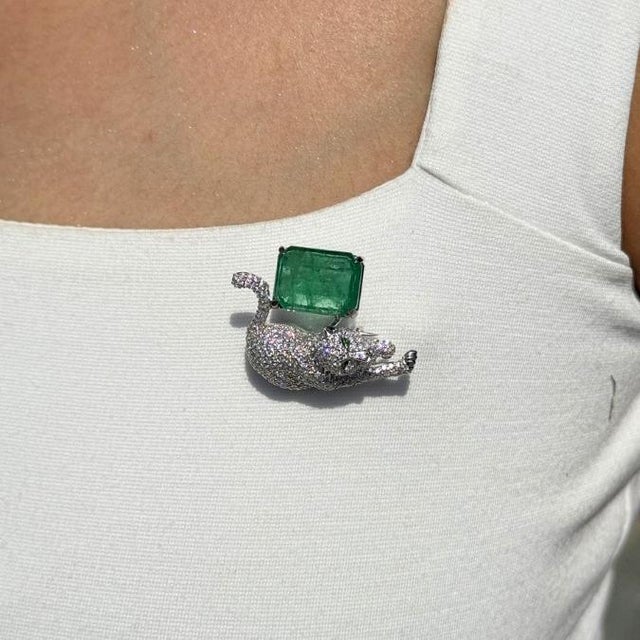This panther brooch features a vibrant 6.49 carat emerald set in 14K white gold. The emerald measuring approximately 10.2...
