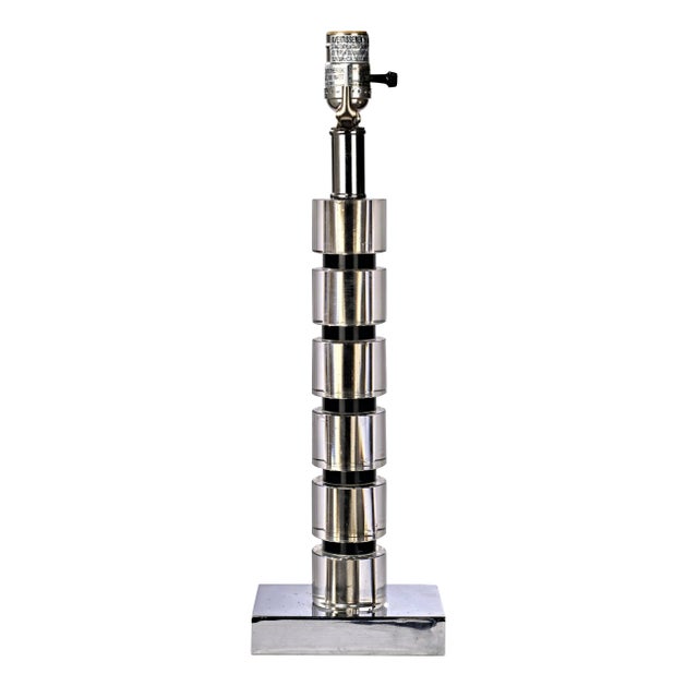 Six elliptical clear lucite pieces are stacked and separated by 5 pieces of black lucite sitting on a square silver...