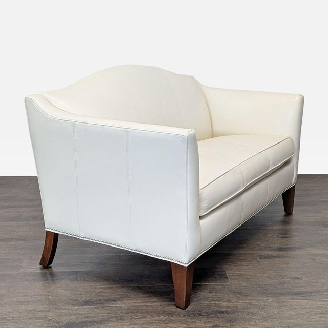 This Ethan Allen loveseat features smooth cream leather upholstery, silver nailhead trim and sturdy wood legs. Its compact...