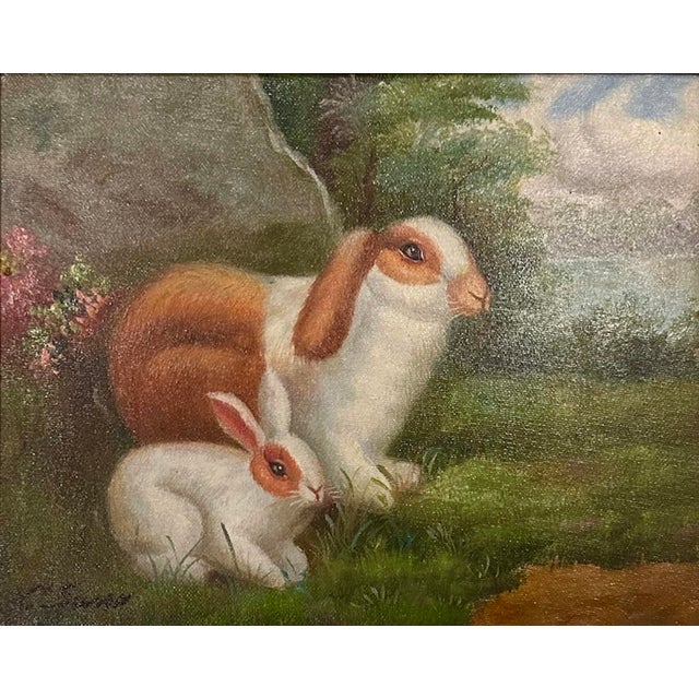 A vintage, gilt framed oil on canvas painting. Features a pair of bunnies surrounded by an English country landscape....