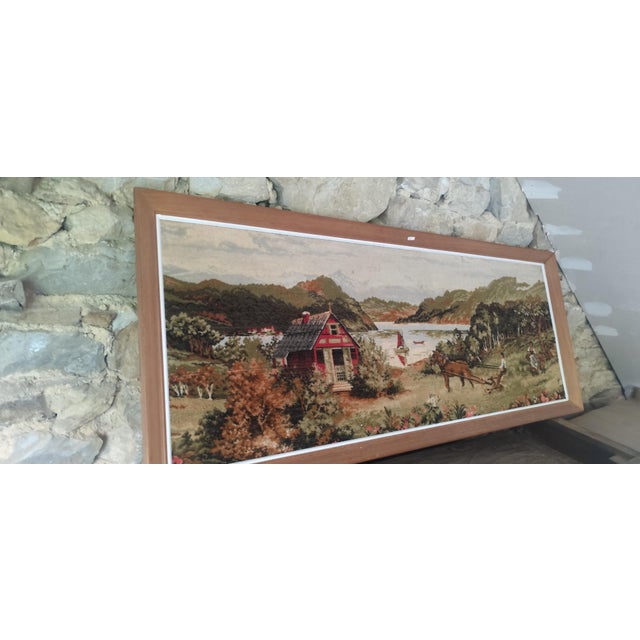 A striking large-format framed textile artwork depicting a peaceful Nordic countryside scene with a traditional red...