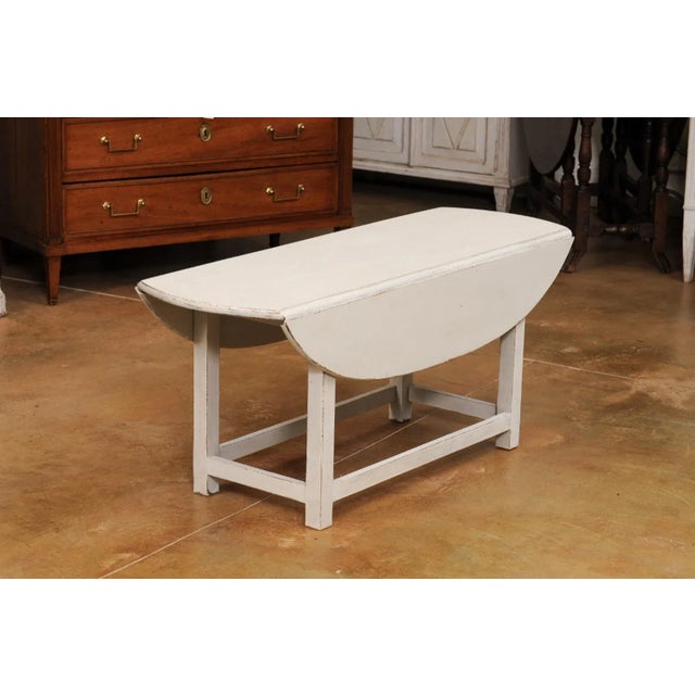 A Swedish oval painted coffee table with two drop leaves, straight legs and plain cross stretchers. Introducing a piece of...