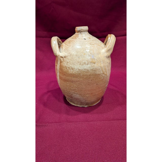 A 19th-century utilitarian stoneware jug featuring an early wheel-thrown ovoid form and two hand-applied loop handles. The...