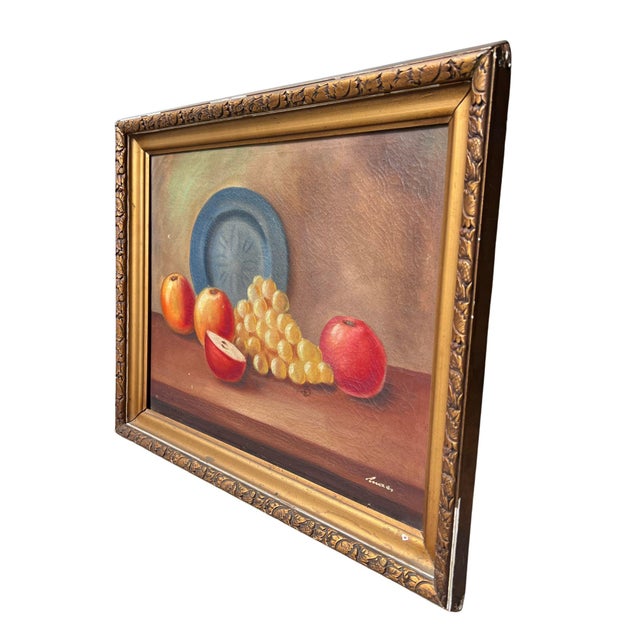 Circa 1940, an oil still life of fruit on a tabletop, set in an ornate gilt frame with a carved leaf-and-acorn motif. The...