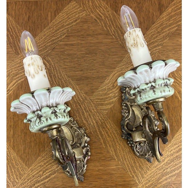 A beautiful pair of Vintage French sconces featuring ornate brass wall mounts combined with elegant decorative porcelain...