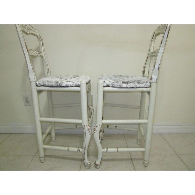 Two elegant Mid Century Rustic French barstools in white with a shabby chic design. They feature rush seat straw and are...
