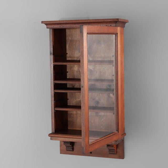 A 20th-century hanging curio cabinet, crafted from walnut wood. This display piece features a single glass-front door,...