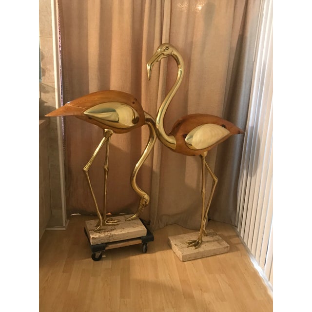 Pair of nearly five-foot tall stylized brass and wood Flamingos on travertine bases. Both have a hidden compartment and...