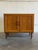 This compact storage unit features a sleek profile accented by framed cabinet doors. It rests gracefully on tapered wooden...