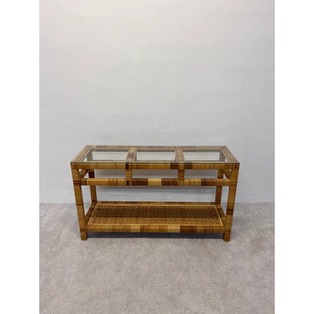 Woven rattan console table with glass top from the 1970s. The lower shelf has a rattan chevron pattern and top shelf is...