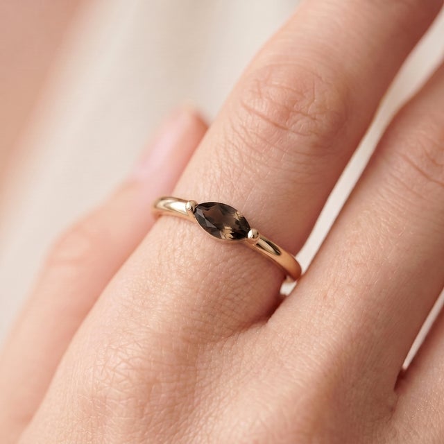 A subtle, minimalist solitaire featuring an earthy smoky-brown marquise-cut quartz set in an east-west orientation, held...