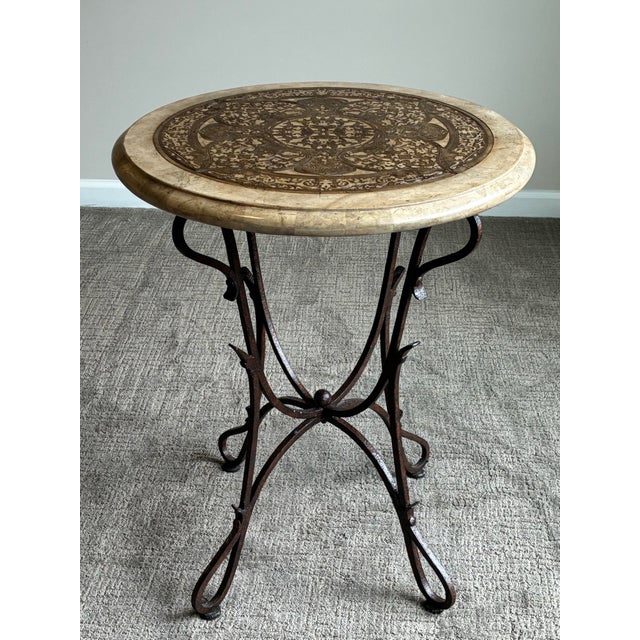 An elegant Mediterranean-inspired accent table featuring a richly detailed decorative inlaid top set above a sculptural...