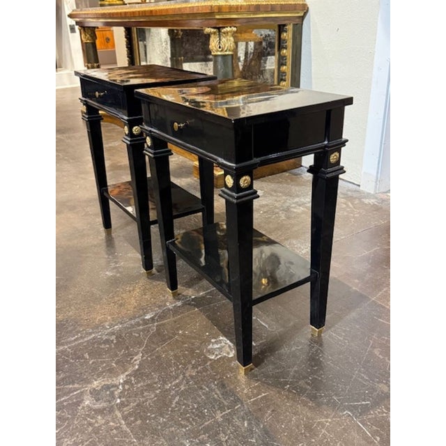 This product is a pair of antique black lacquered Jansen Manner side tables with brass details. These side tables are...