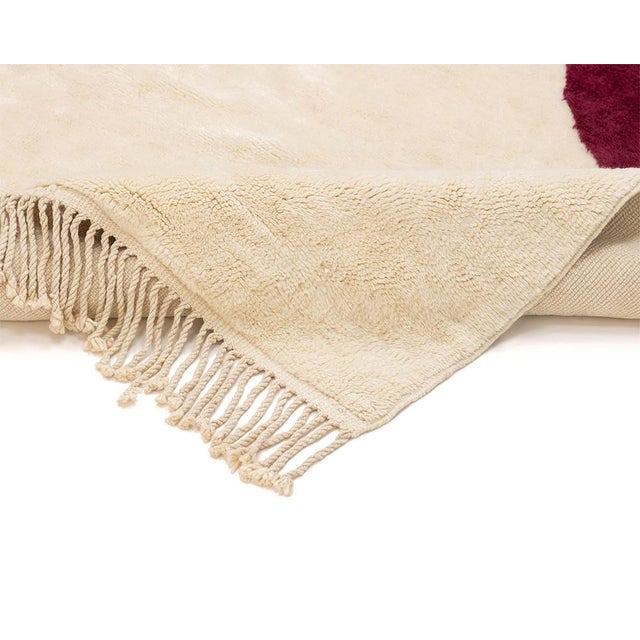 Minimalist hand-knotted wool rug, artfully contrasting an Ivory base with deep red abstract forms, creates a striking and...