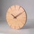 A modern-style wooden wall clock with a round face made from a single piece of light-colored natural wood with a distinct...