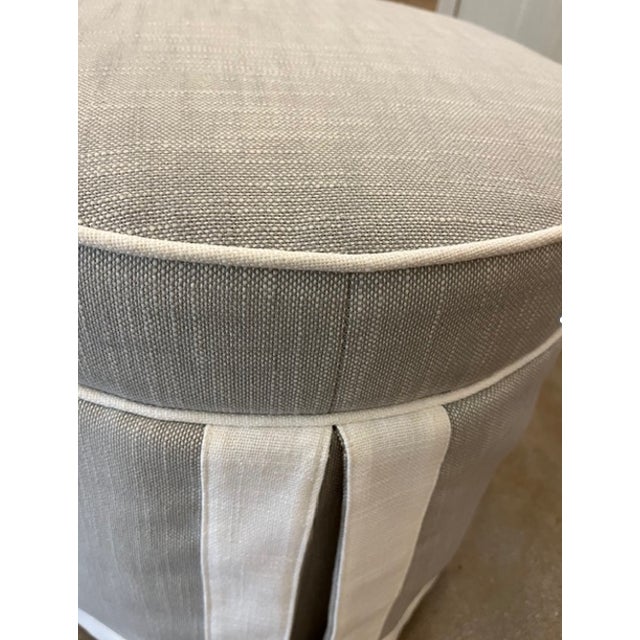 This round ottoman includes a welted and boxed cushion atop a long kick pleat skirt. Greige linen with Natural linen welt...