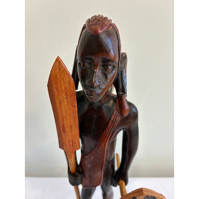A vintage hand-carved wooden Maasai warrior sculpture featuring a traditional spear and shield. This artisan-crafted...