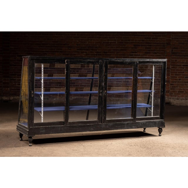 Large antique wood-framed general store display case with a black-painted finish and slanted glass front. The floor-...