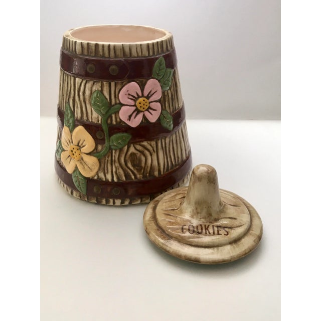 A charming mid century rustic cookie jar in the form of an old fashioned churn with a pair of pastel flowers, covered in a...