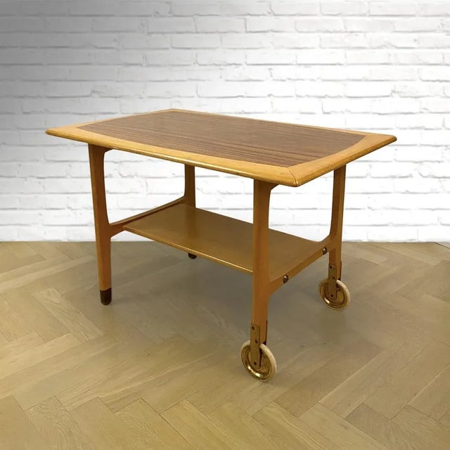 A Swedish mid-century serving table, made from solid beech wood and walnut veneer. Two legs on casters, the other two with...