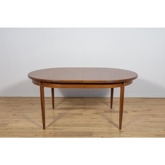 This is an oval-shaped teak dining table manufactured by G-Plan in the 1960s. The table has reinforced edges of the top....