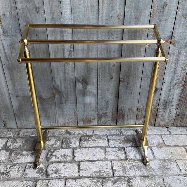 A handsome piece of vintage brass bathroom furniture — a freestanding three-bar towel or blanket rack, raised on tapered...