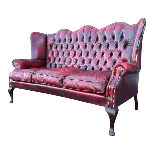 English high-back Chesterfield sofa in burgundy leather with deep button tufting, rolled arms, and nailhead trim. Raised...