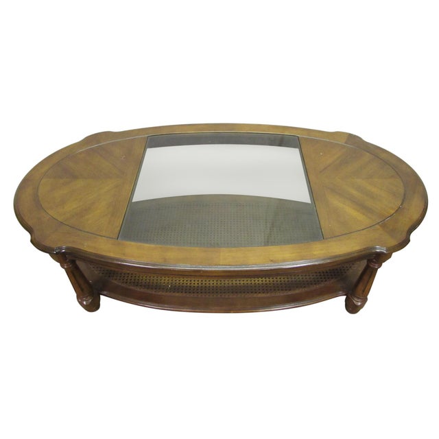 Oak oval shaped coffee table with a cutout glass center and four post legs. The second shelving level has a caning...
