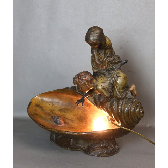 Terracotta sculpture depicting two children perched on a large seashell, one of them trying to catch a small mollusk. This...