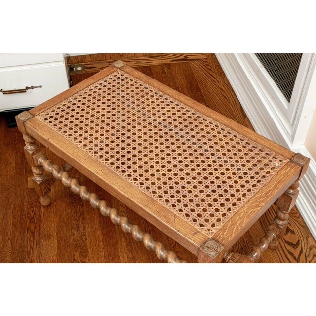 A rectangular, antique English cane bench with an oak frame that rises on block and barley twist turned legs and...
