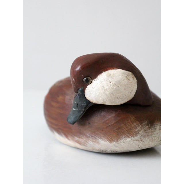 A vintage hand-carved and hand-painted canvasback duck decoy by Jim Gibbs, dated 1984, with a low, rounded form and a...