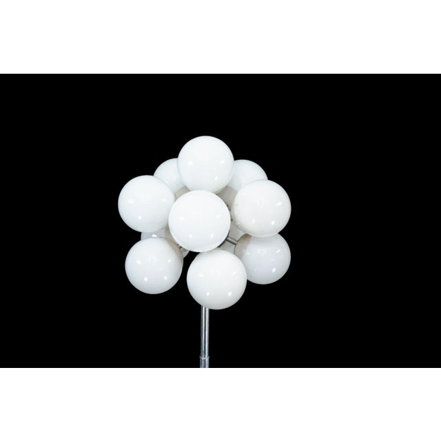 The lamp features eleven white glass globes arranged in a compact radial cluster at the top of a slender chrome-plated...