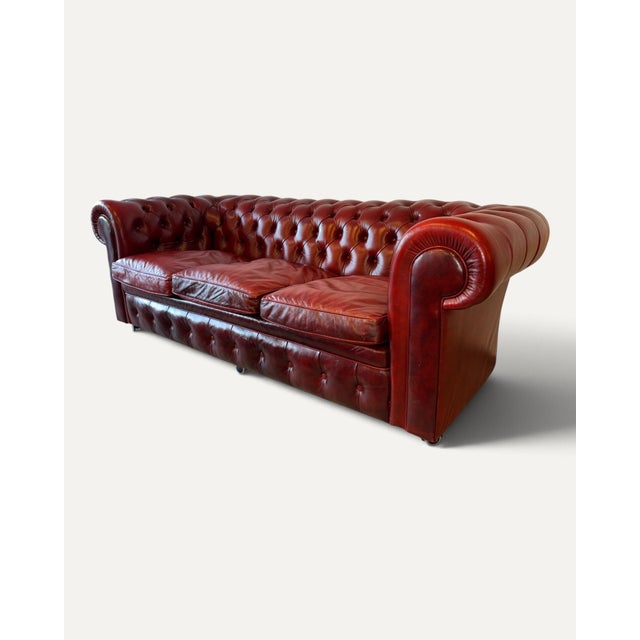 Classic three-seater Chesterfield sofa in genuine oxblood leather with deep button tufting and rolled arms. Three loose...