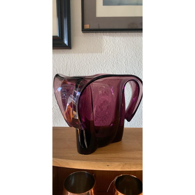 A striking vintage amethyst art glass vase featuring a bold sculptural silhouette with gracefully folded ribbon-like...