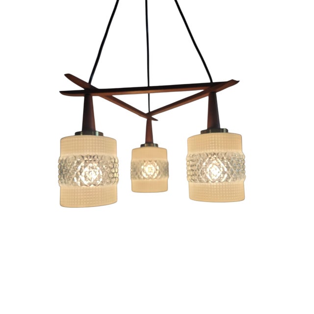 A three-light pendant lamp that presents a harmonious composition of brass, teak, and glass. This elegant lighting fixture...