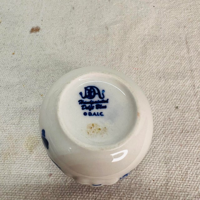 Delft blue toothpick holder featuring a pig with its head stuck in the fence on the front, pigs rear on the back. Floral...