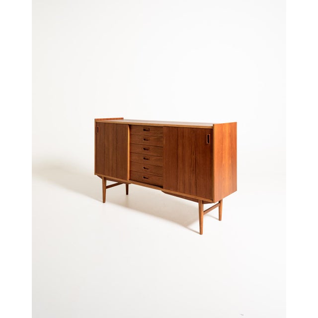 Teak highboard with two side compartments, six central drawers, and oak details. Shaped handles and tapered legs....