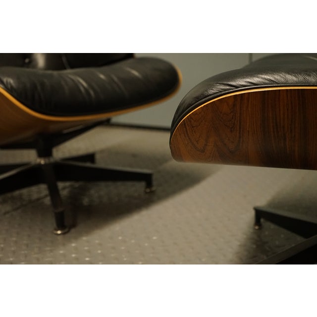 A lovely Eames Lounge chair and ottoman in black leather. The shell of the chair is walnut and the shell on the ottoman is...