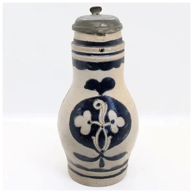 DETAILS An antique Westerwald beer pitcher of baluster form with cobalt brushed decoration. The hinged pewter lid with...