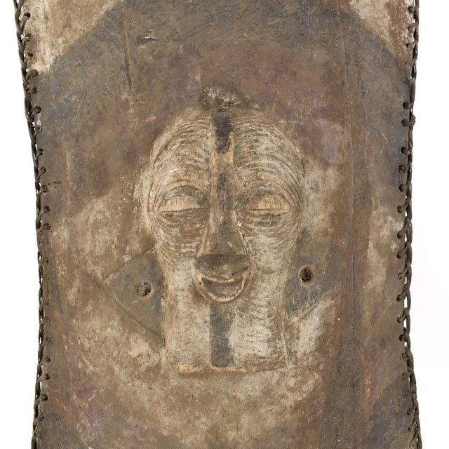The wooden shield featuring a Kifwebe mask at its center was prevalent in the Songye region during colonial and pre-...