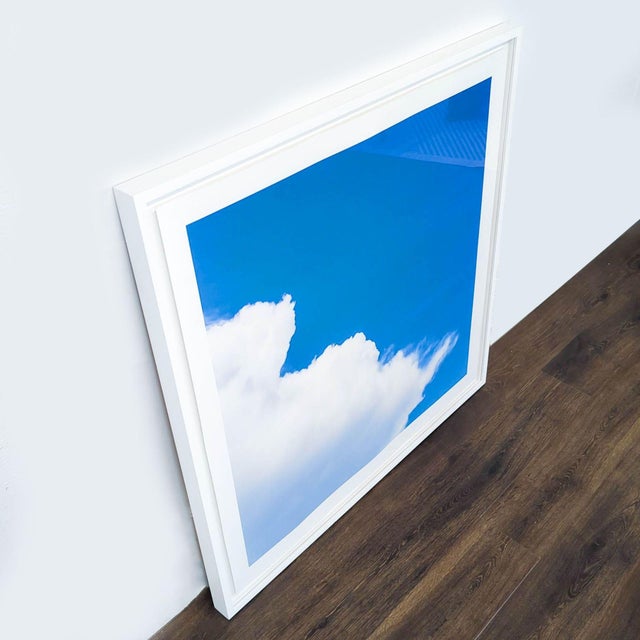 This is a vibrant print showing a bright blue sky with fluffy white clouds. The artwork comes in a modern white frame....