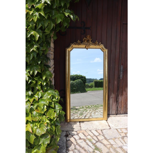 Large Louis XV style mirror, entirely gilded with gold leaf. Its upper pediment is richly decorated with scrolls, foliage,...