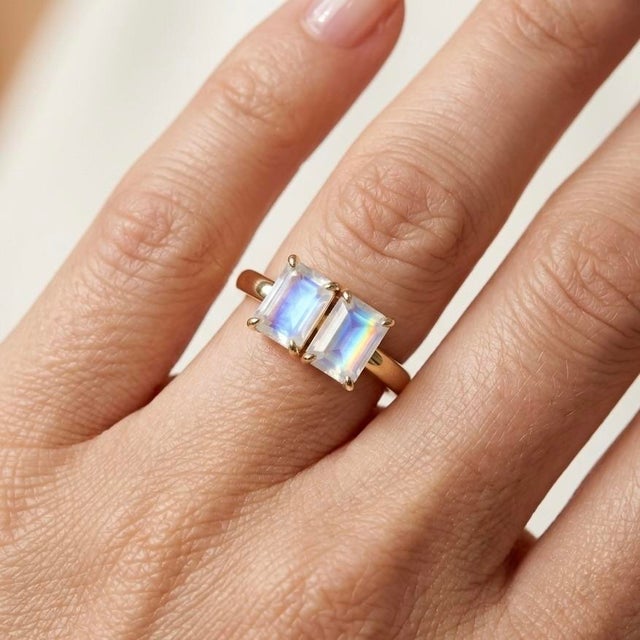 Captivating and ethereal, this stunning Toi et Moi ("You and Me") ring features a striking duo of emerald-cut Rainbow...
